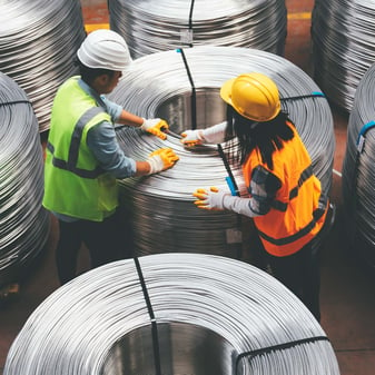 Two people standing over metal coils in the metal manufacturing plant