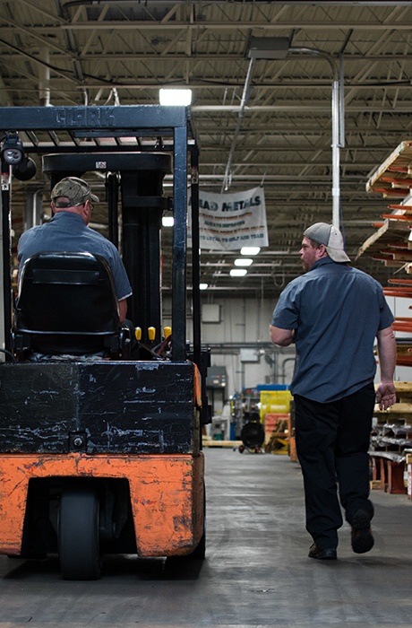 Two warehouse employees - one on fork lift and another walking alongside talking